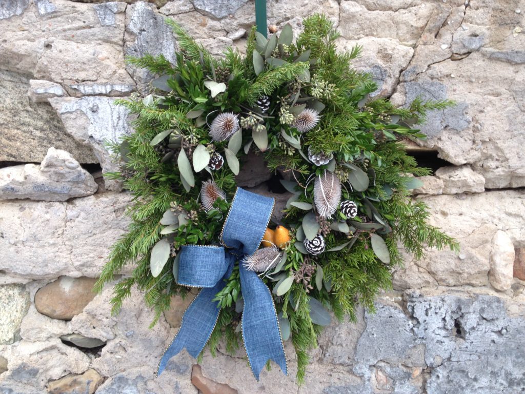 A large premium greens mix comprised of mountain hemlock, American boxwood tips, seeded eucalyptus with 5 white redpine cones, 5 white painted teasels, 2 mini yellow faux pears, finished with a premium blue bow. Cost $123.00